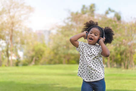Happy african little girl have big smile, her listening music with headphones and  dancing at...