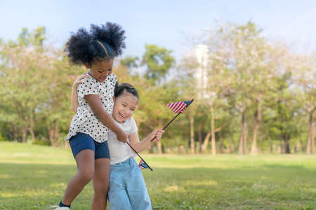 African american and caucasian mix girls playing and hold a american flag at outdoors park, Ethnic girls , Relationship little kids, Diverse ethnic concept.の写真素材