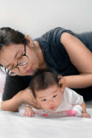 Little two month asian baby lying on stomach and try raised her neck, Asian mother come to help her daughter,  Family concept.;の写真素材