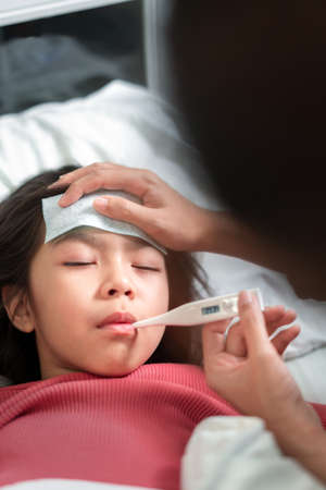 Asian mother touch hand young daughter for encouragement, mother measuring temperature girl with digital thermometer, Sick child have  high fever, Selective focus, Healthy and infection conceptの写真素材