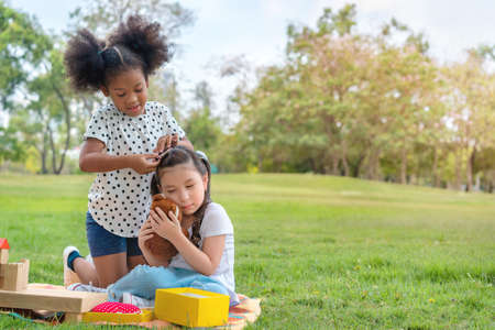 African girl helping to put hairpin clip on caucasian girl friend  after play together, Relationship little kids, Diverse black and white ethnic concept.の写真素材