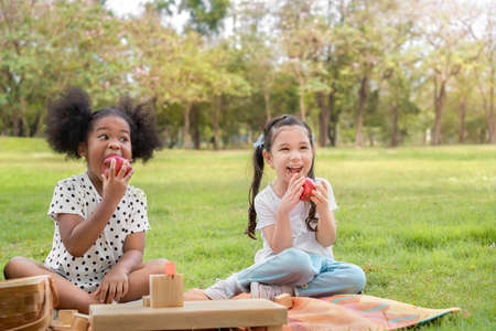 Happy cheerful white girls and black girl lying on mat and drawing with pencil on her book at outdoors park, education concept.の写真素材