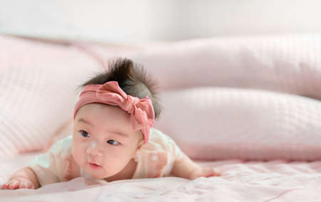 Asian babe girl 5 month with pink bow lying on stomach at bedroom.の写真素材