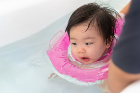 Asian little baby girl swimming and wear rubber ring on neck in bathtub, Mother holding daughter for safety support, Living lifestyle family indoors concept.の写真素材
