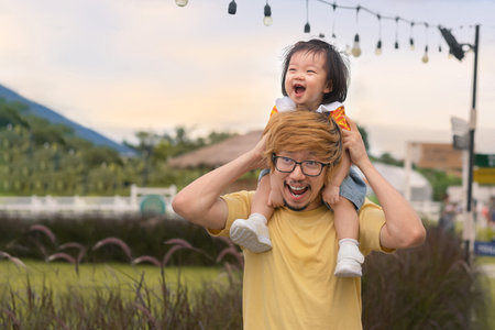 Happy asian father carrying smile asian daughter on neck at park, Piggyback activity, Family relations concept.の写真素材