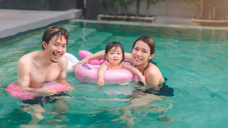 Asian little baby girl swimming and wear rubber ring  in pool, Mother and father holding daughter for safety support, Living lifestyle family indoors concept.の写真素材
