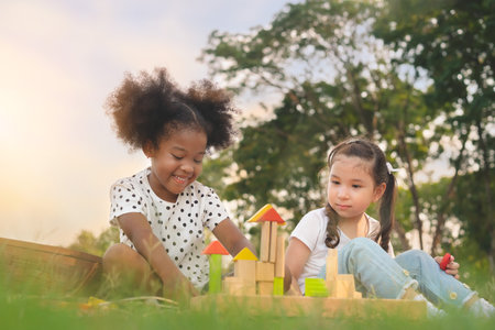 Happy cheerful ethnic girls play wooden block puzzle together at outdoors park , Relationship little kids, Diverse ethnic concept.の写真素材