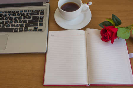 red rose,opened notebook, cup of coffee and pen on wooden office desk.の写真素材