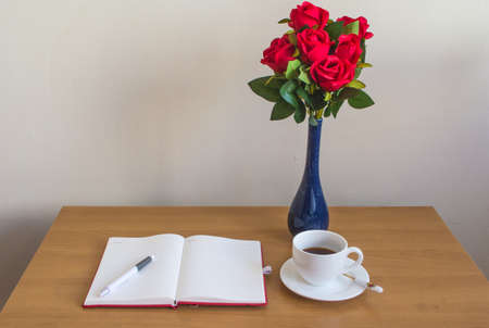 red roses,opened notebook, cup of coffee and pen on wooden office desk.の写真素材