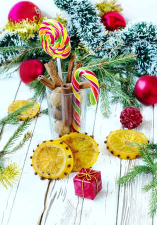 cinnamon sugar candies orange nuts in a glass on a white wooden background with firtree branches tinsel and ballsの写真素材