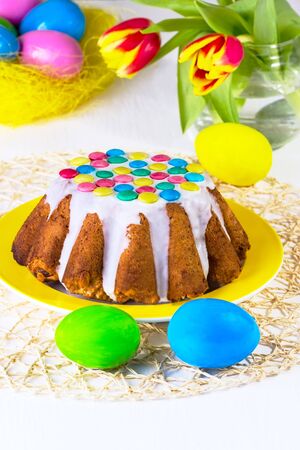 Easter cake with white glaze on a yellow plate on a wattled napkin on a white background with color...