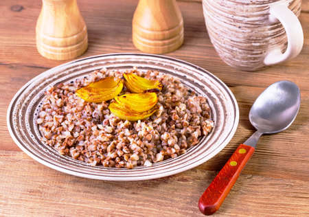 buckwheat cereal with the baked onions in a brown plate on a brown wooden backgroundの写真素材