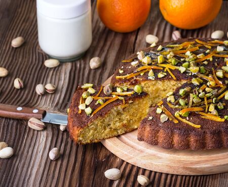 sweet pie with pistachios and a dried peel of orange on a round wooden board on a brown wooden backgroundの写真素材