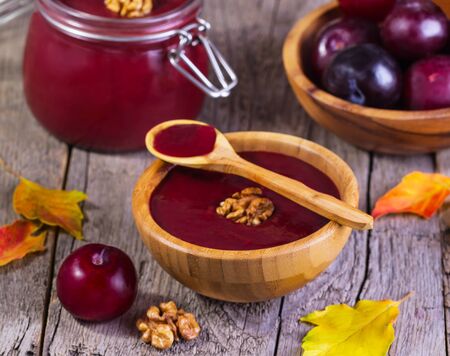 jam with plums and walnuts in a brown wooden plate on a wooden backgroundの写真素材