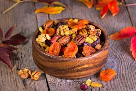 nuts and dried fruits in a brown wooden plate on a wooden background with autumn leavesの写真素材