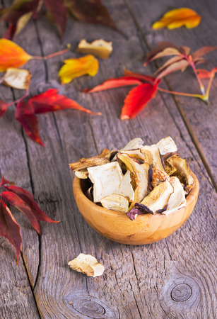 dried-up cepes in a brown wooden plate on a wooden background with autumn leavesの写真素材