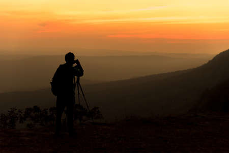 Silhouette of traveler when he is taking photograph on mountain at sunrise.の写真素材