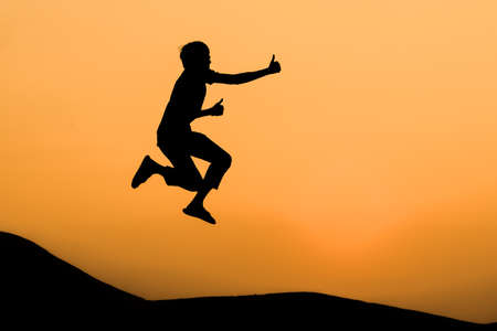 silhouette of man in happy jumping and thump up on orange sunset sky