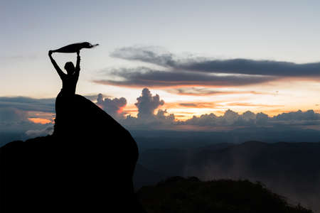 Silhouette of women spreading hand on the top of mountain at sunsetの写真素材