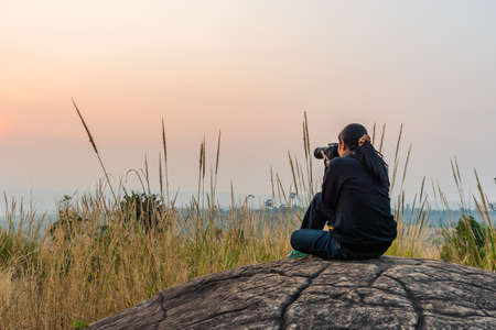 Woman sitting on the rock and taking a photographの写真素材