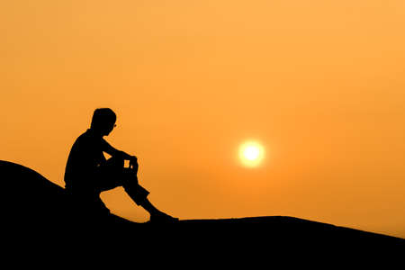 Silhouette of sitting man on rock at sunset.の写真素材