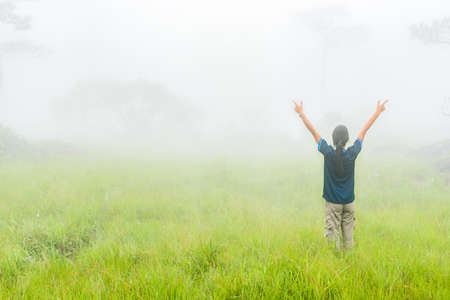 Happy young woman risning hand and enjoying misty day on green meadow.の写真素材