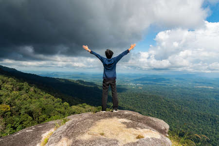 Young successful man open arms on mountain peak above the forest.の写真素材