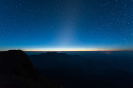 Stars illuminated above the dark silhouette mountain before sunrise.の写真素材