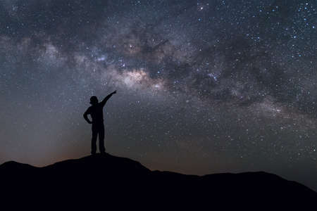 Milky Way landscape. Silhouette of Happy woman standing on top of mountain with night sky and bright...