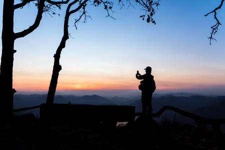 Mae Ping river view point. Silhouette woman taking a mountain sunrise photograph by mobile phone.の写真素材