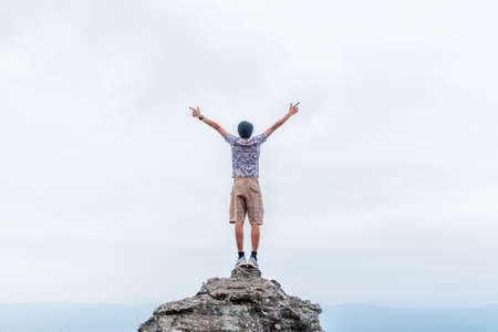 Young man stay on rock and spreading hand for enjoying sky view.の写真素材