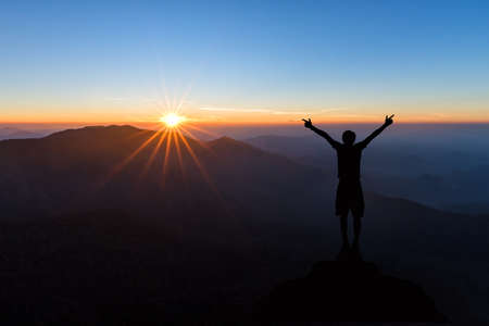 Silhouette of man spreading hand and enjoy to see sunrise above the mountains in Kanchanaburi,...