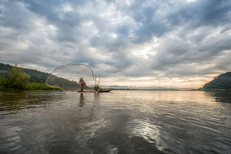 Fisherman on boat in action when fishing of fish trap on Mekong riverの写真素材