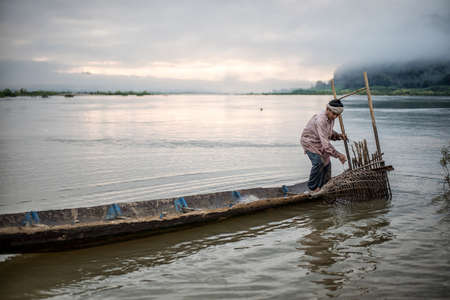 Fisherman on boat in action when fishing of fish trap on Mekong riverの写真素材