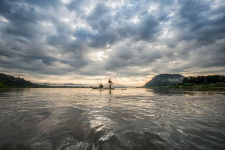 Fisherman on boat in action when fishing of fish trap on Mekong riverの写真素材