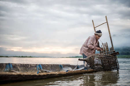Fisherman on boat in action when fishing of fish trap on Mekong riverの写真素材