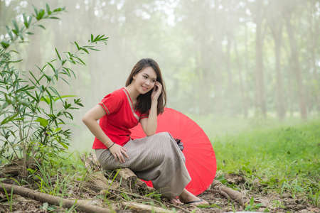 Beautiful Thai girl in Lanna traditional costume with red umbrella. Lanna culture in Northern Thailandの写真素材