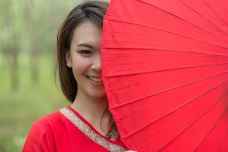 Beautiful Thai girl in Lanna traditional costume with red umbrella. Lanna culture in Northern Thailandの写真素材