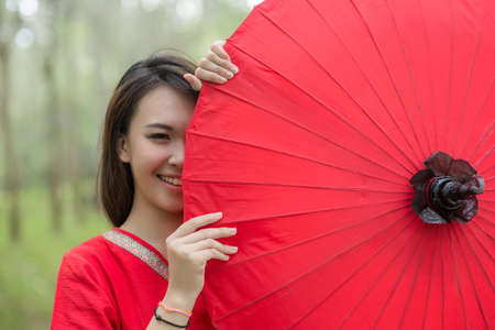 Beautiful Thai girl in Lanna traditional costume with red umbrella. Lanna culture in Northern Thailandの写真素材