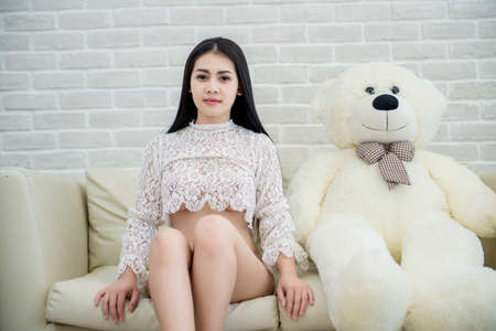 Beautiful woman in a white lingerie sitting on white a chair in room with brick wallの写真素材