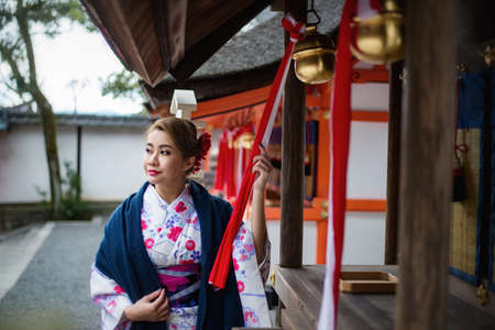 Woman dressed in traditional japanese costume walking under tori gates at the fushimi-inari shrine, Kyoto Japanの写真素材