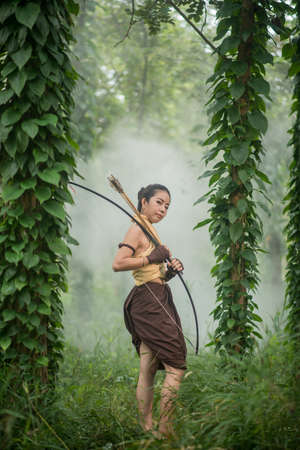 Beautiful Thai woman archer with longbow and arrows in forest background vintage style at Thailandの写真素材