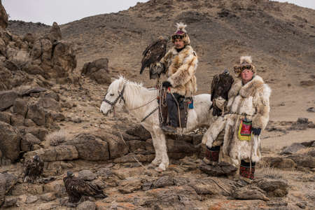 Thailand tourist in Mongolia traditionally riding horse with Kazakh Eagle Hunter in a desert...