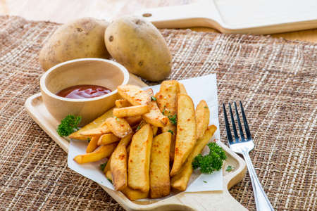 Tasty french fries on cutting board with ketchup, on wooden table background
