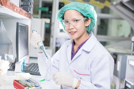 Portrait of a female researcher working in a lab scientist using microscope with colleague working...