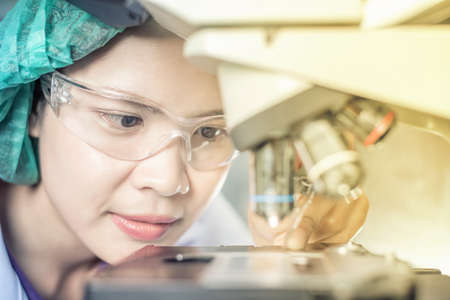 Portrait of a female researcher working in a lab scientist using microscope with colleague working in backgroundの写真素材