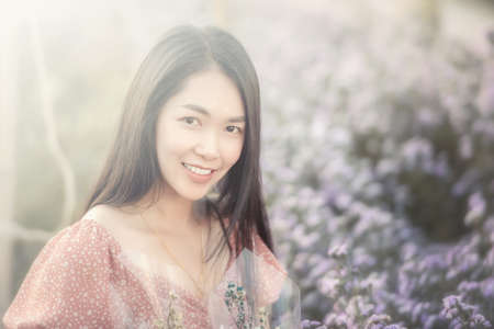 Beautiful young woman traveler looking flowers field sitting on a blurred flowers garden background. Travel holiday relaxation concept. の写真素材