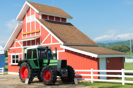 Green Tractor and Red Barn with blue sky and white fence.のeditorial素材
