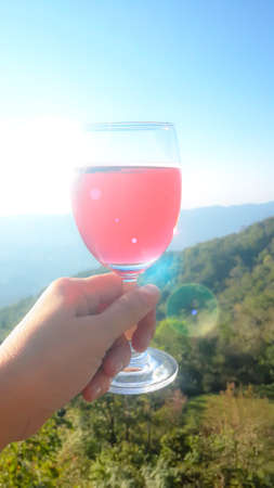 Phot of a glass of solf drink on hand, moutain backgound blur, relax concept.の写真素材