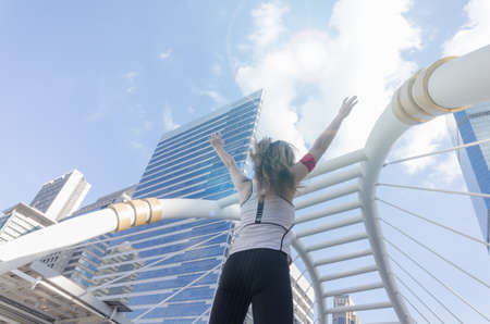 Young lady turn back and raise her hand up to sky in sport wear in the city.の写真素材